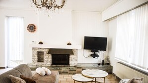 Una sala de estar con chimenea, sofá, televisor y candelabro.