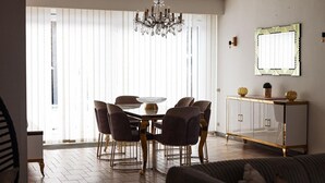 Un comedor con una araña, una mesa redonda y seis sillas. Hay un aparador con adornos en la parte superior.