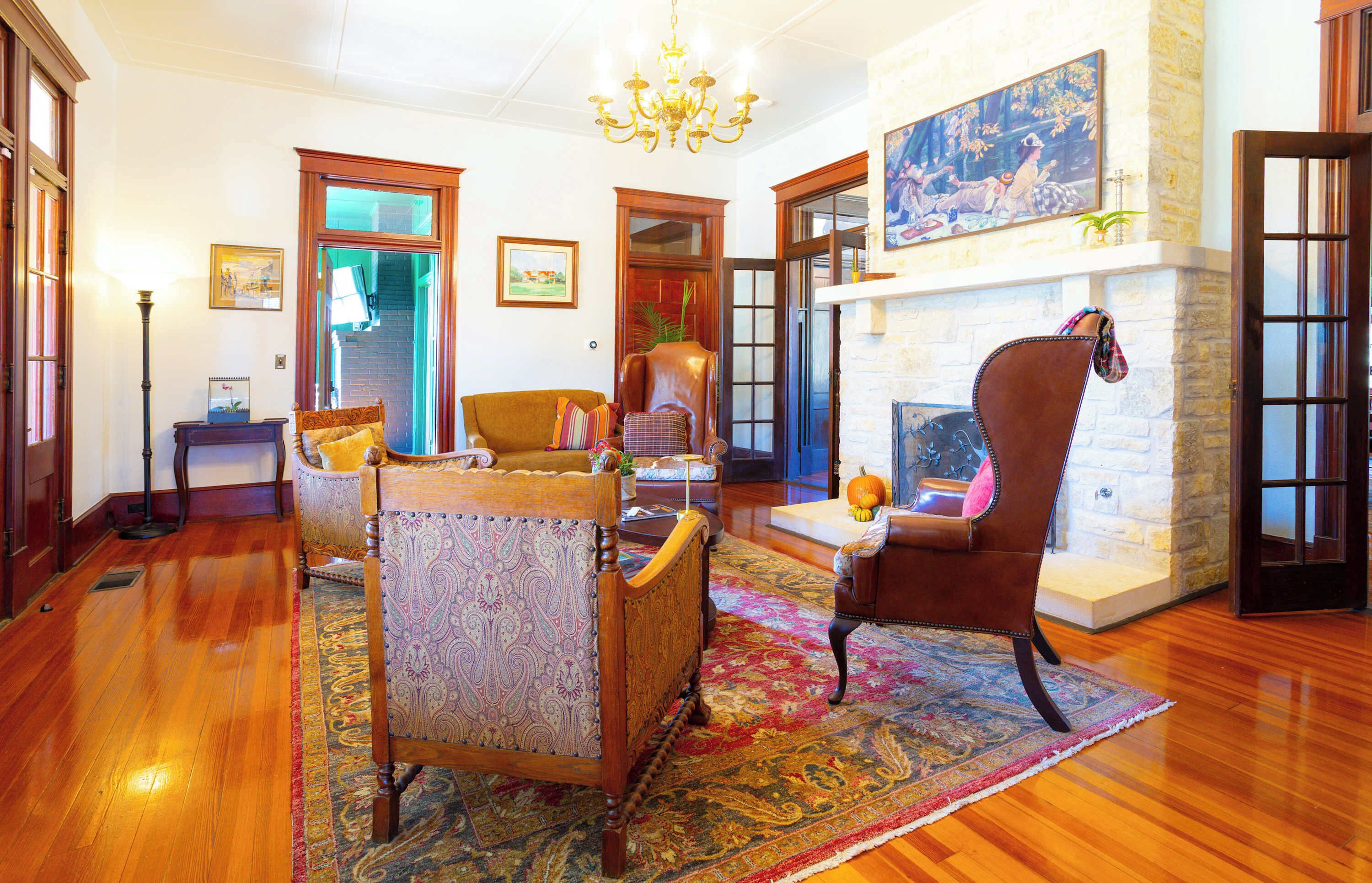 Uma sala de estar ampla com piso de madeira, um tapete grande e uma lareira. Há várias poltronas e um sofá dispostos para sentar.