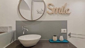 Une salle de bain moderne avec un grand lavabo ovale, un miroir rond et un panneau mural portant l’inscription « Smile ».