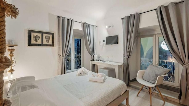 Une chambre d’hôtel comprenant un lit, un bureau, une chaise et un balcon avec des rideaux.