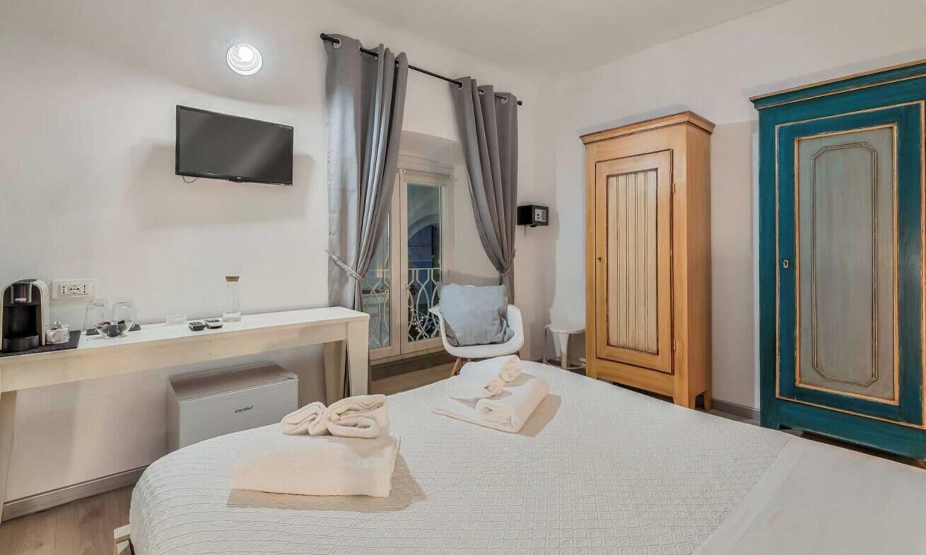 Hotelkamer met een bed, bureau met een flatscreen televisie, een kledingkast en een badkamer zichtbaar door een glazen deur.