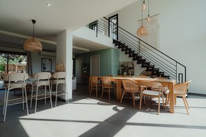 A spacious dining area with a high ceiling, a staircase, and modern lighting fixtures.