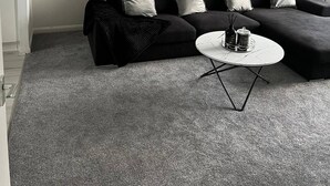 Een moderne woonkamer met een zwart hoekbank, een witte salontafel en een grote spiegel aan de muur.