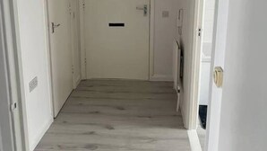 Een gang met witte wanden en een houten vloer die naar een gesloten deur leidt.