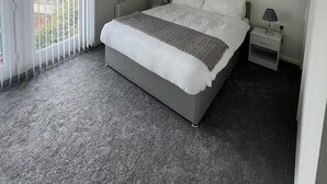 Een slaapkamer met een bed, twee nachtkastjes, een plafondlamp en uitzicht door een raam met jaloezieën.
