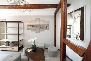 A modern living room with a wooden ceiling, a large window, a bookshelf, and a wall-mounted artwork. - Chez Anne Sophie – Historic Center – Full Comfort (Colmar)
