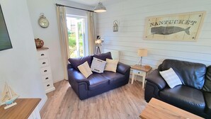 Ein gemütliches Wohnzimmer mit zwei Ledersofas, einem Holztisch, einem Beistelltisch mit Lampe und einer Wanduhr.