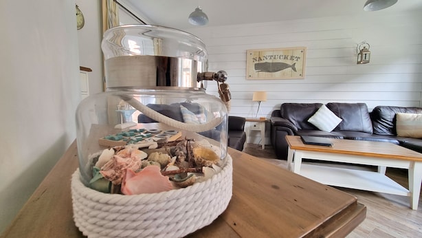 Ein Wohnzimmer mit einem Glas-Terrarium auf einem Holztisch, einem schwarzen Ledersofa, einem weißen Couchtisch und einer Wanduhr.