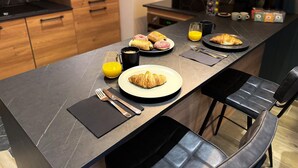 Une cuisine moderne avec un coin petit-déjeuner comprenant des croissants, un verre de jus d’orange et une machine à café.