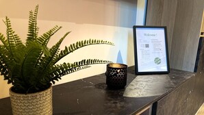 Un comptoir d’accueil agrémenté d’une pancarte de bienvenue encadrée, d’une fougère en pot et d’un porte-bougie décoratif.
