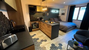 Un espace de vie compact comprenant un coin cuisine, un espace repas et une chambre.