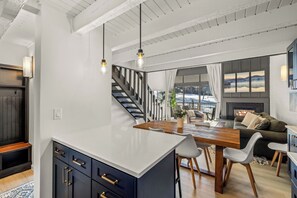 A modern kitchen with a central island, wooden dining table, and a staircase leading to an upper level. - Snowy Ski Basecamp | Fireside + Hot Tubs (Steamboat Springs)