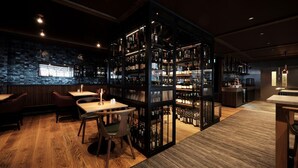 A bar area with wooden flooring, tables, chairs, and a wine rack with bottles. - Houmbgaarden (Roros)