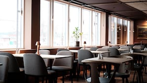 Un ristorante con diversi tavoli e sedie, ampie finestre e una pianta in vaso.