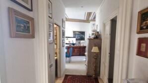 Un couloir avec une porte en arc donnant sur une pièce où se trouvent un téléviseur, un fauteuil et une lampe.