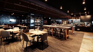 A restaurant with multiple tables and chairs, a bar area with shelves of bottles, and a kitchen in the background. - Osloveien 6 (Roros)