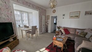 Un salon comprenant un téléviseur, un canapé, une table basse et un coin repas avec des chaises et une table.