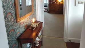 Un couloir avec un papier peint à motifs, une console en bois sur laquelle est posée une bougie allumée, un miroir et un tableau encadré accroché au mur.