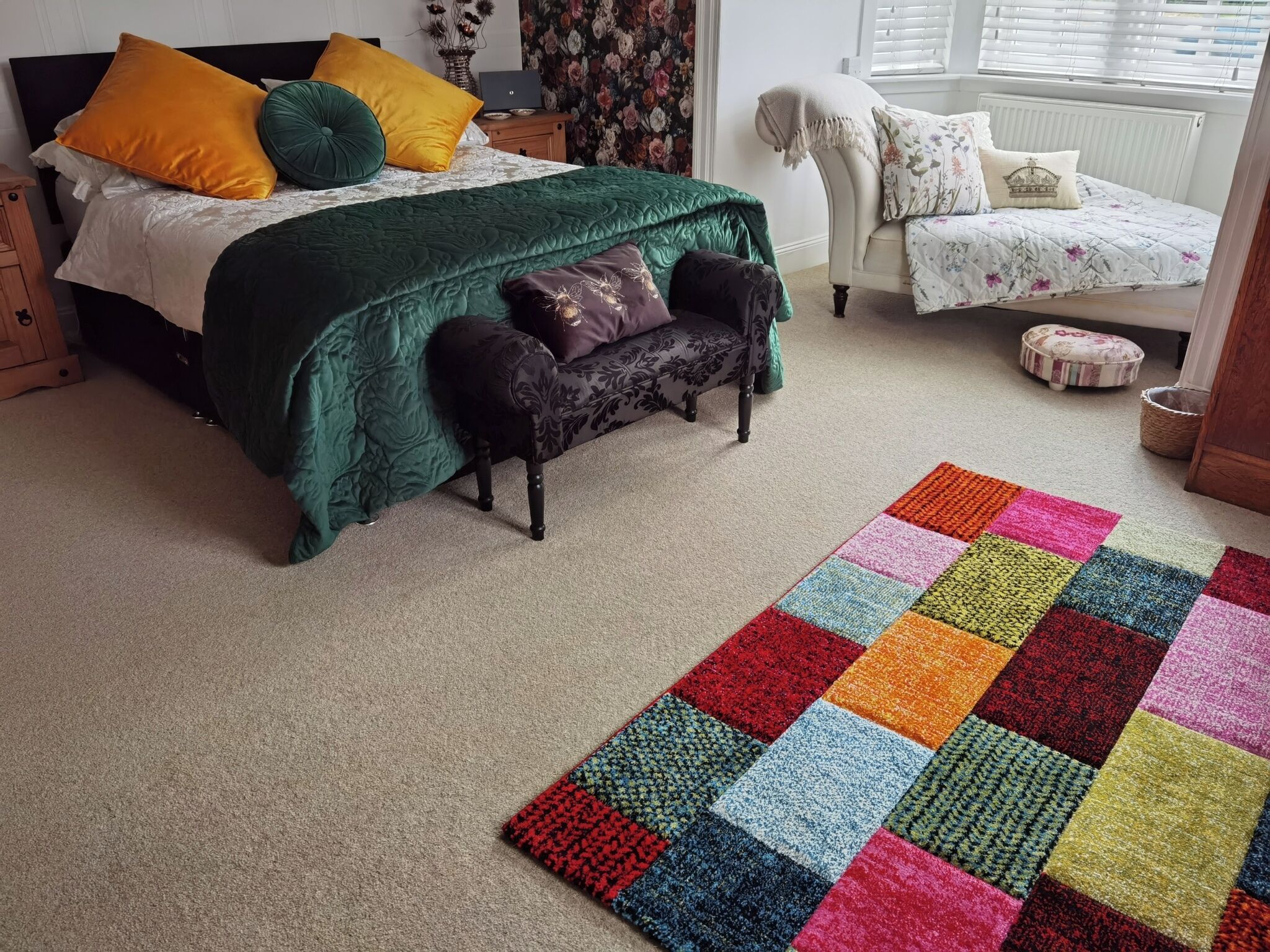 A bedroom with a bed, a bench, a colorful rug, and a chair.