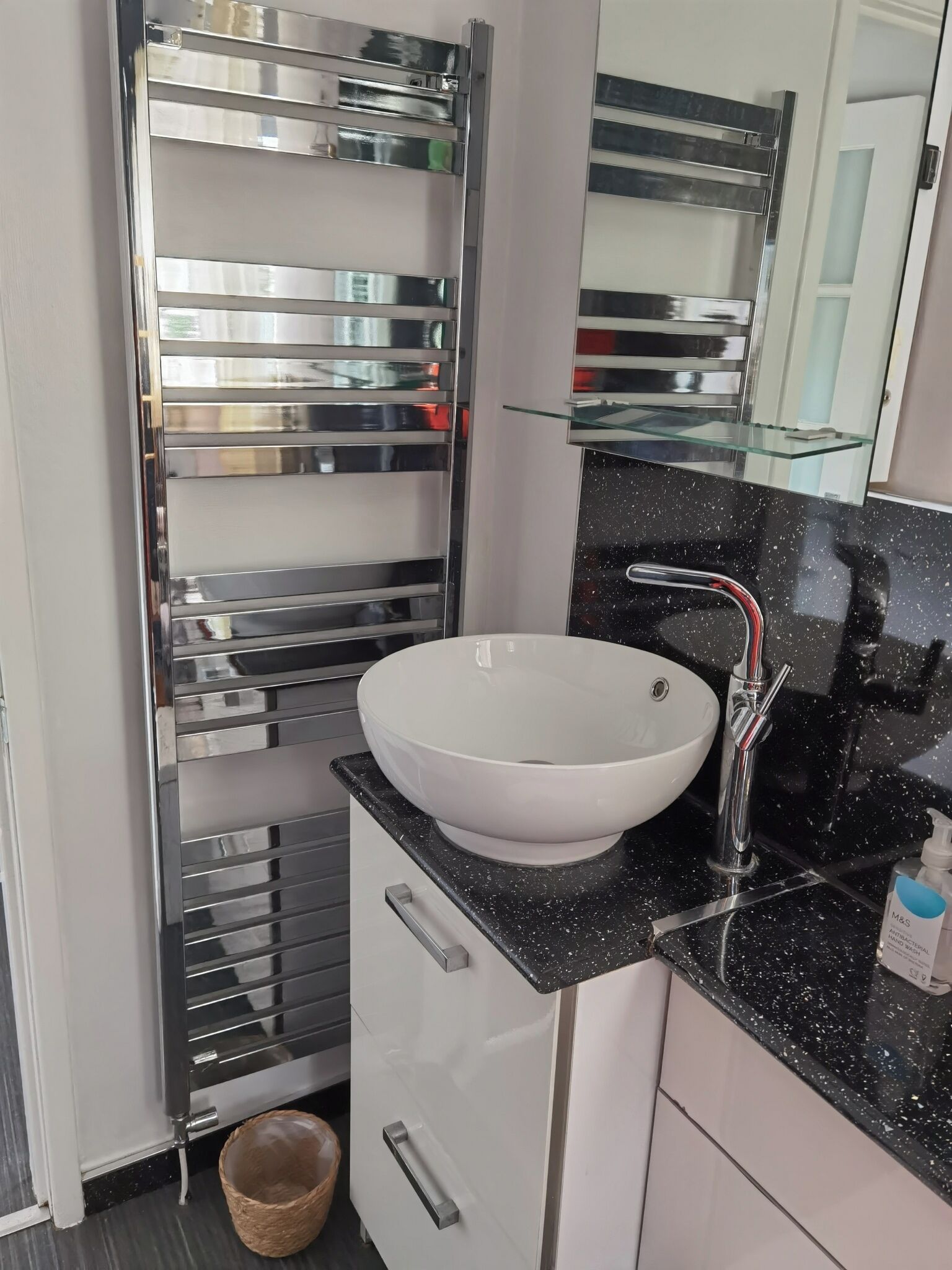 Une salle de bain moderne avec un lavabo blanc, un porte-serviettes chromé et une étagère en verre.
