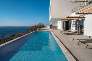 A modern pool with a clear view of the sea, a patio with lounge chairs, and a minimalist building design. - NEW! Stylish Villa Collina - Stunning Sea Views, Private Pool, Top amenities (Duće)