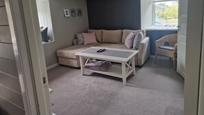 A cozy room with a sectional sofa, a small table, a wicker chair, and a window with a view. - Room-cosy Living Room, Bedroom and Bathr (Askøy)