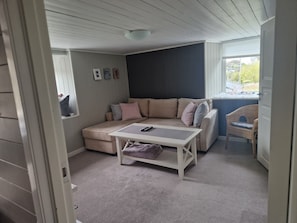 A cozy room with a sectional sofa, a small table, a chair, and a window with a view. - Room-cosy Living Room, Bedroom and Bathr (Askøy)