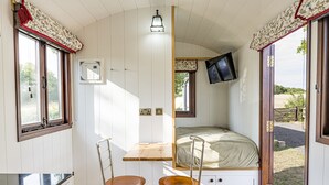 Ett litet rum med en säng, ett litet bord, två stolar, en tv och ett fönster med gardiner.