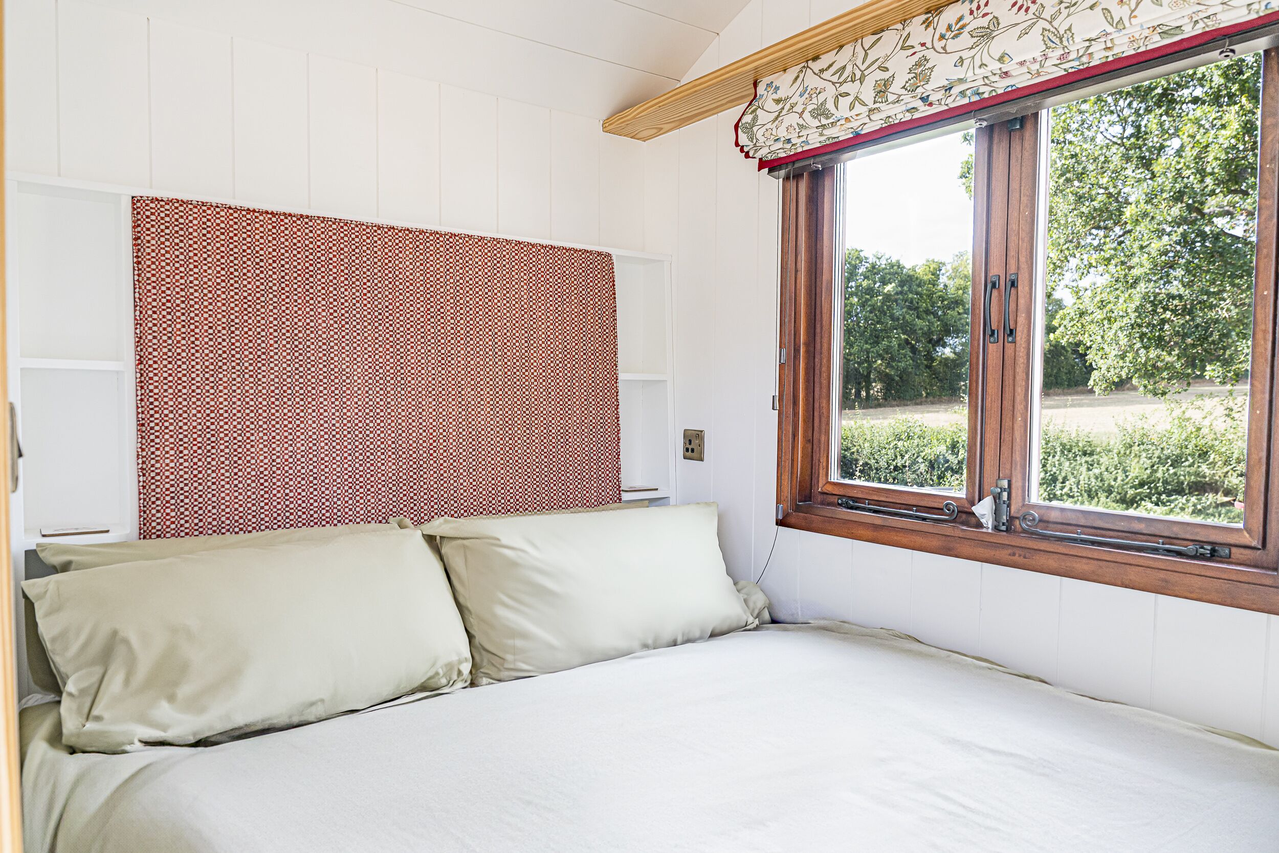 Une chambre à coucher avec un lit, une fenêtre donnant sur un paysage verdoyant et une tête de lit à motifs.