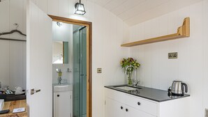 Ett modernt kök med vita skåp, en svart bänkskiva, en trähylla och en duschavdelning med glasväggar.