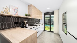 A modern kitchen with a wooden countertop, a coffee machine, and a view of a swimming pool through a glass door. - Benoa Zen Ground-floor luxury, direct pool access, by Oyoostays (Pilar de la Horadada)