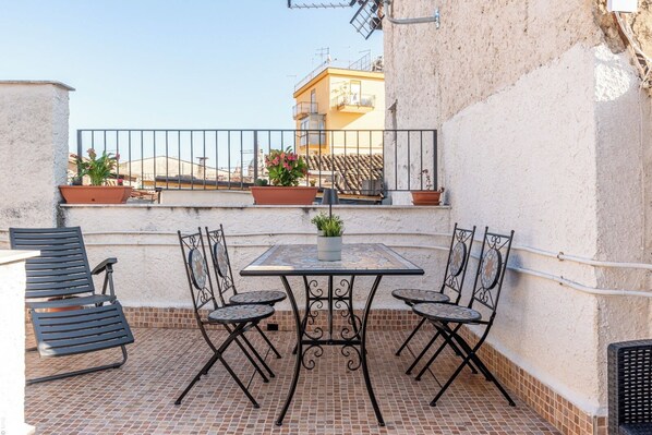 A rooftop patio with a tiled floor, a metal table with chairs, and potted plants. - Casa Peppa by Wonderful Italy (Palermo)