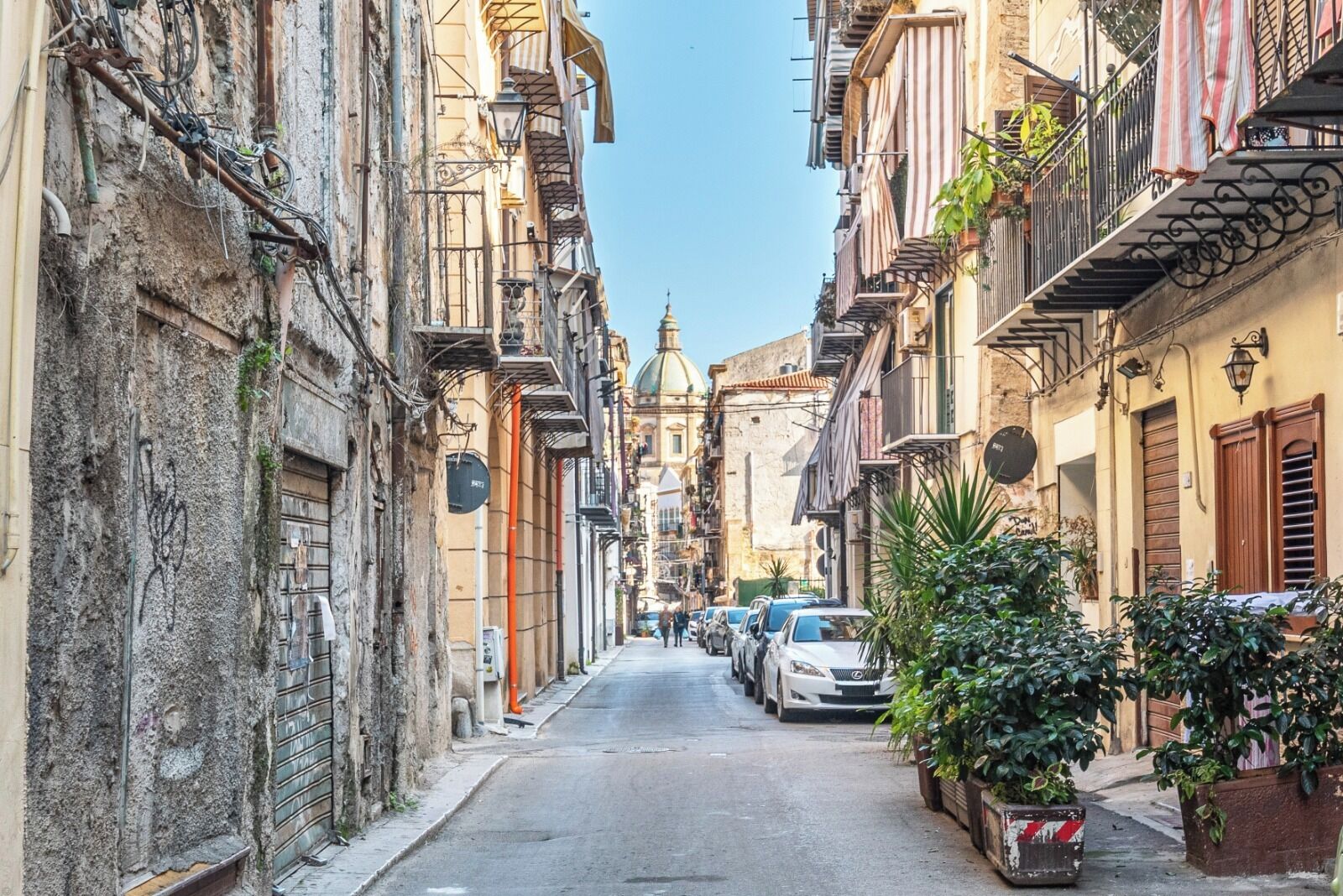 Une rue étroite bordée d’immeubles à plusieurs étages, dont certains sont dotés de balcons et de terrasses.