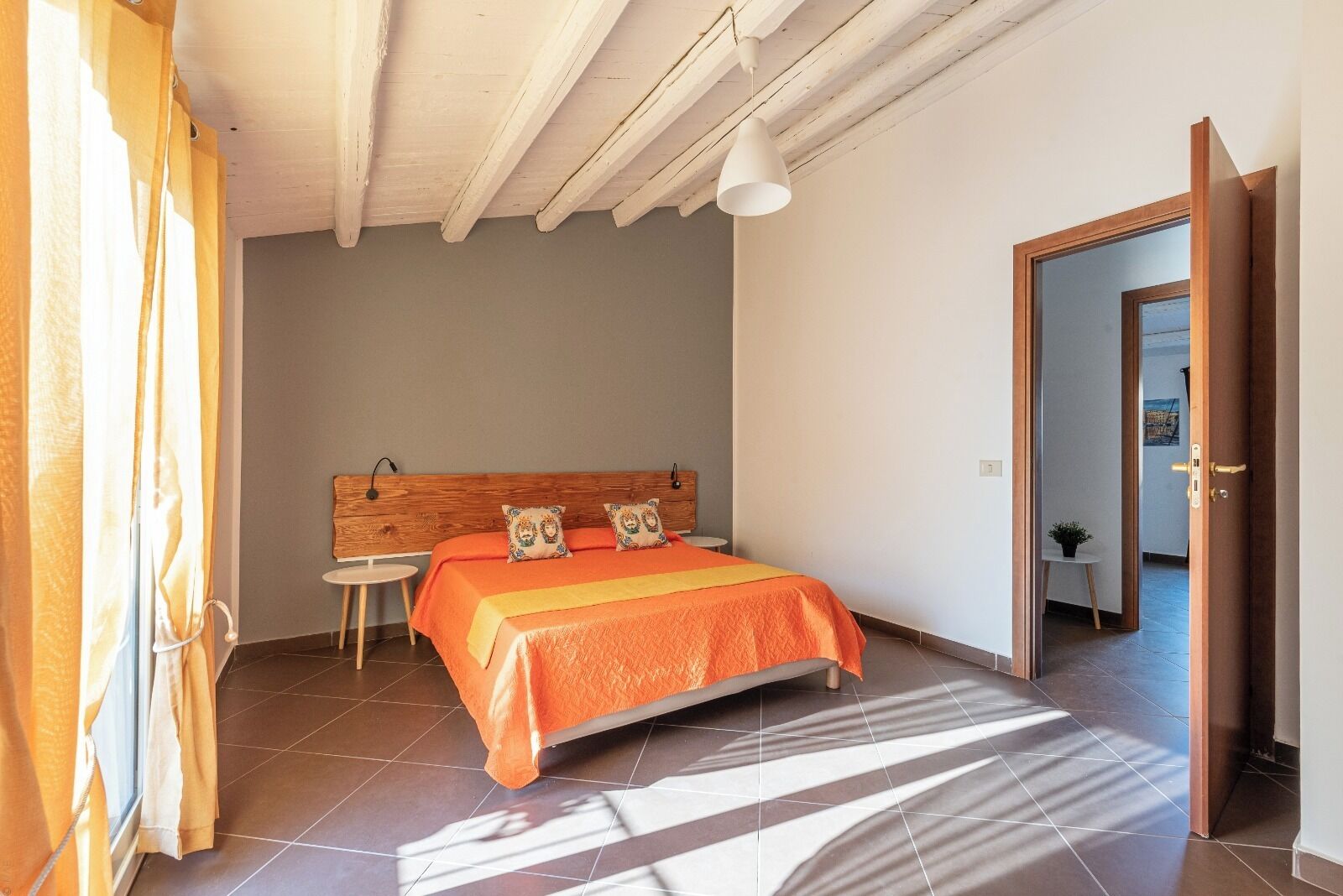 A bedroom with a bed, a wooden headboard, a small table, and a door leading to another room.