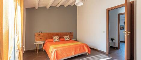 A bedroom with a bed, a wooden headboard, a small table, and a door leading to another room.