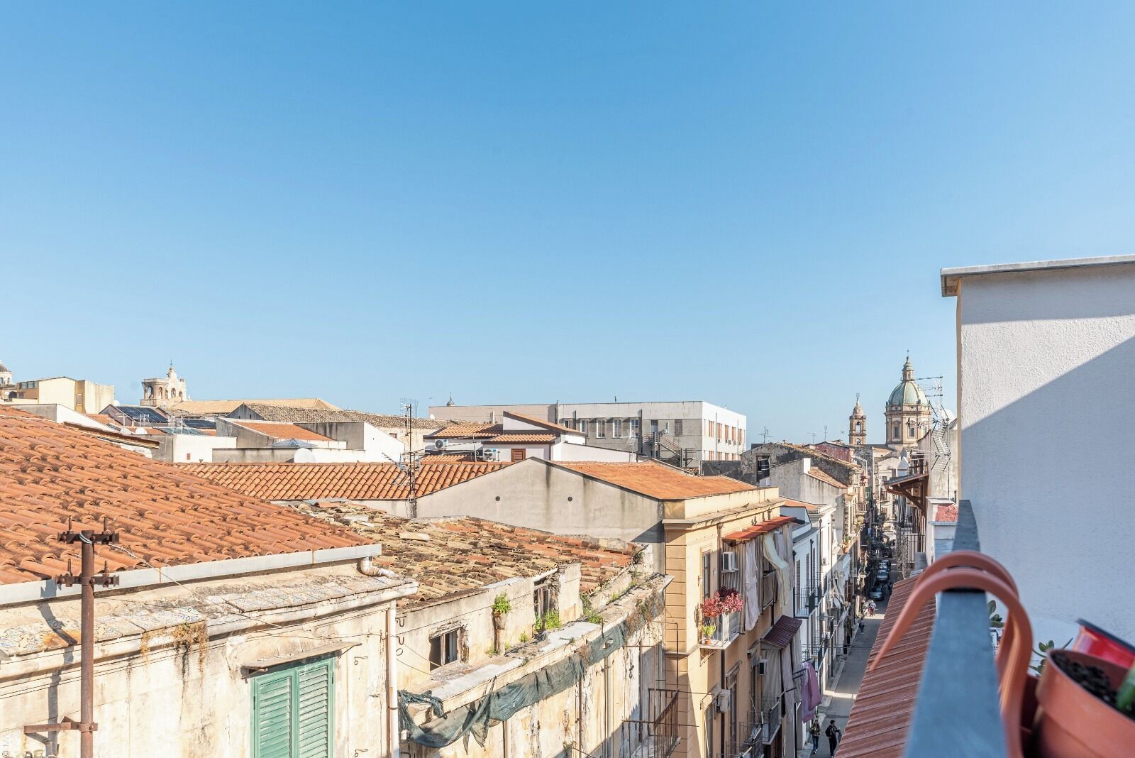 A cityscape with terracotta-tiled rooftops, a mix of historic and modern buildings, and a clear blue sky.