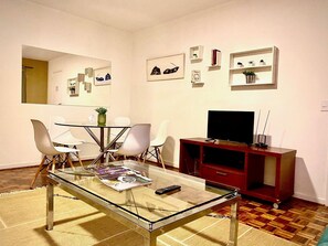 Uma sala de estar moderna com uma mesa de centro de vidro, cadeiras brancas, um móvel de entretenimento vermelho e uma TV de tela plana.