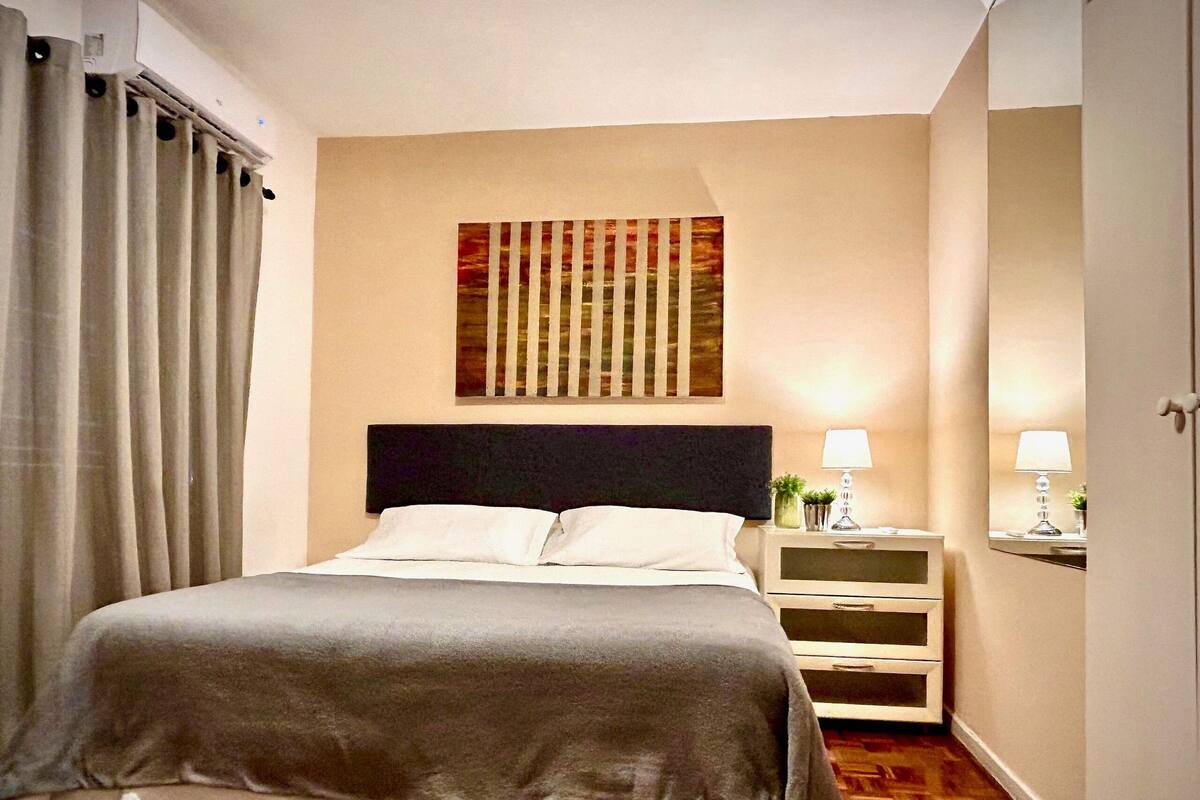 A neatly arranged bedroom with a bed, bedside tables, and a painting on the wall.