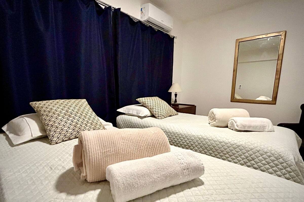 A hotel room with two beds, dark curtains, a mirror, and a bedside lamp.