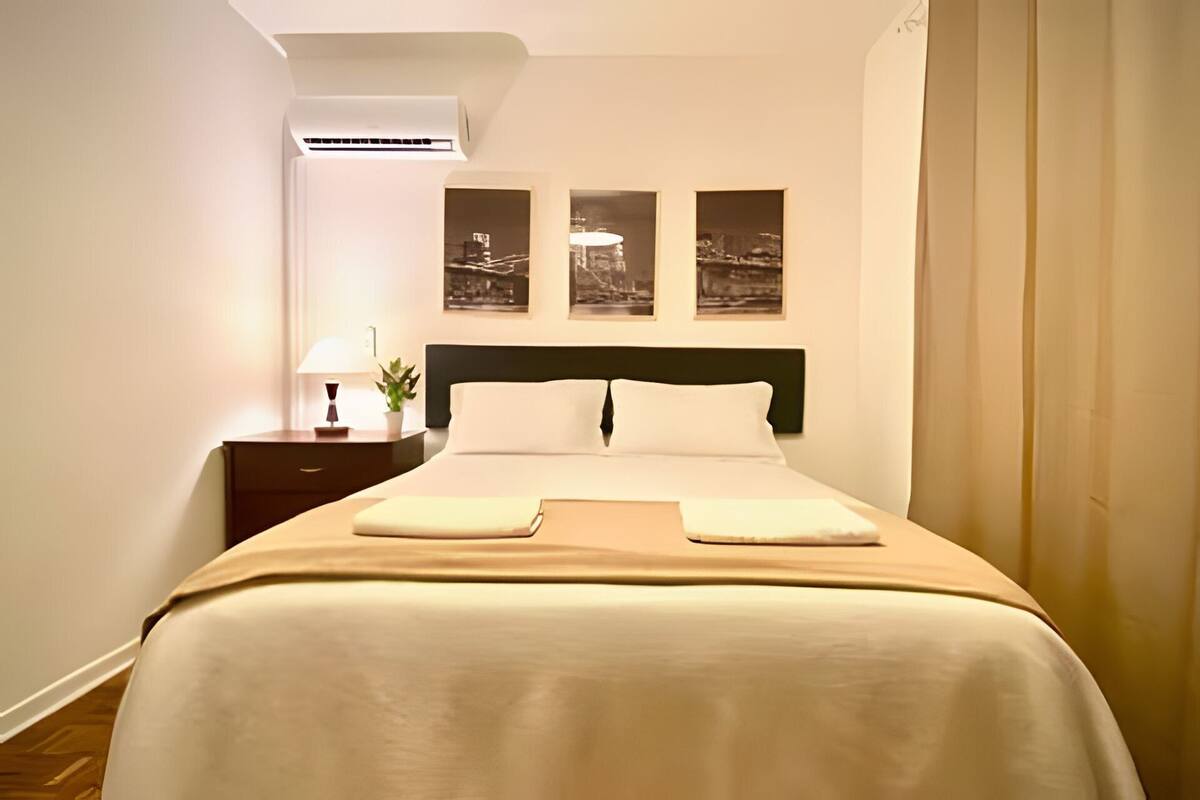 A hotel room with a bed, nightstand, lamp, and three framed pictures on the wall.