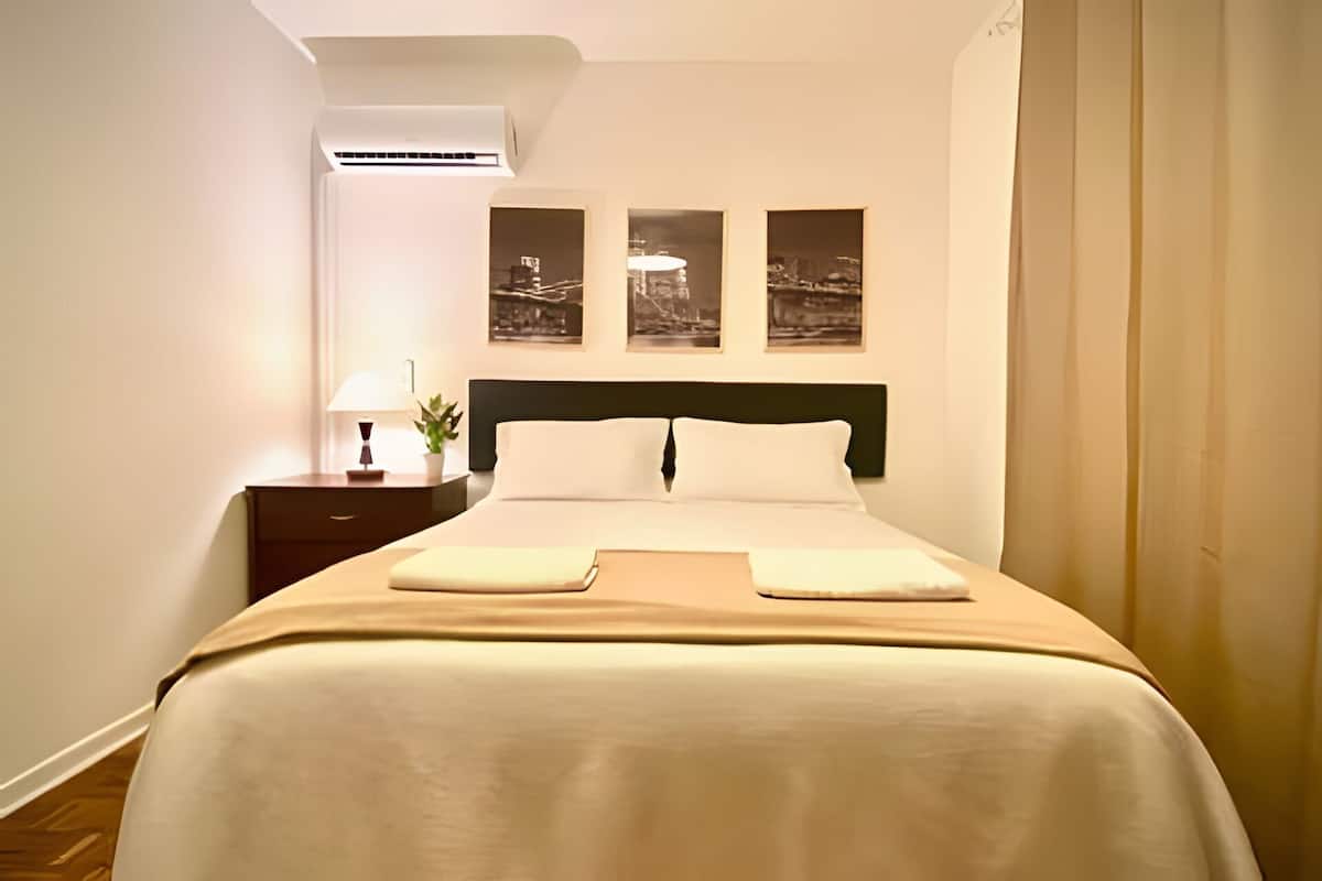 A hotel room with a bed, nightstand, lamp, and three framed pictures on the wall.