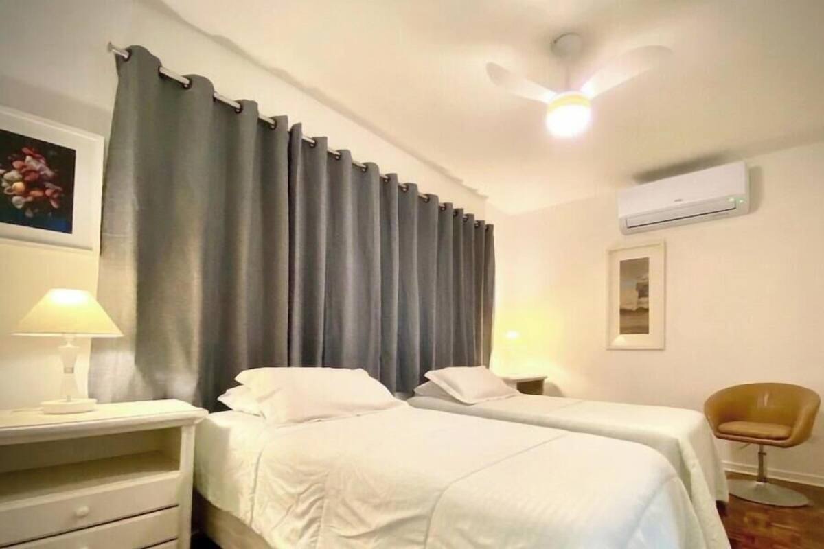 A hotel room with two beds, a chair, a lamp, an air conditioner, and a ceiling fan.