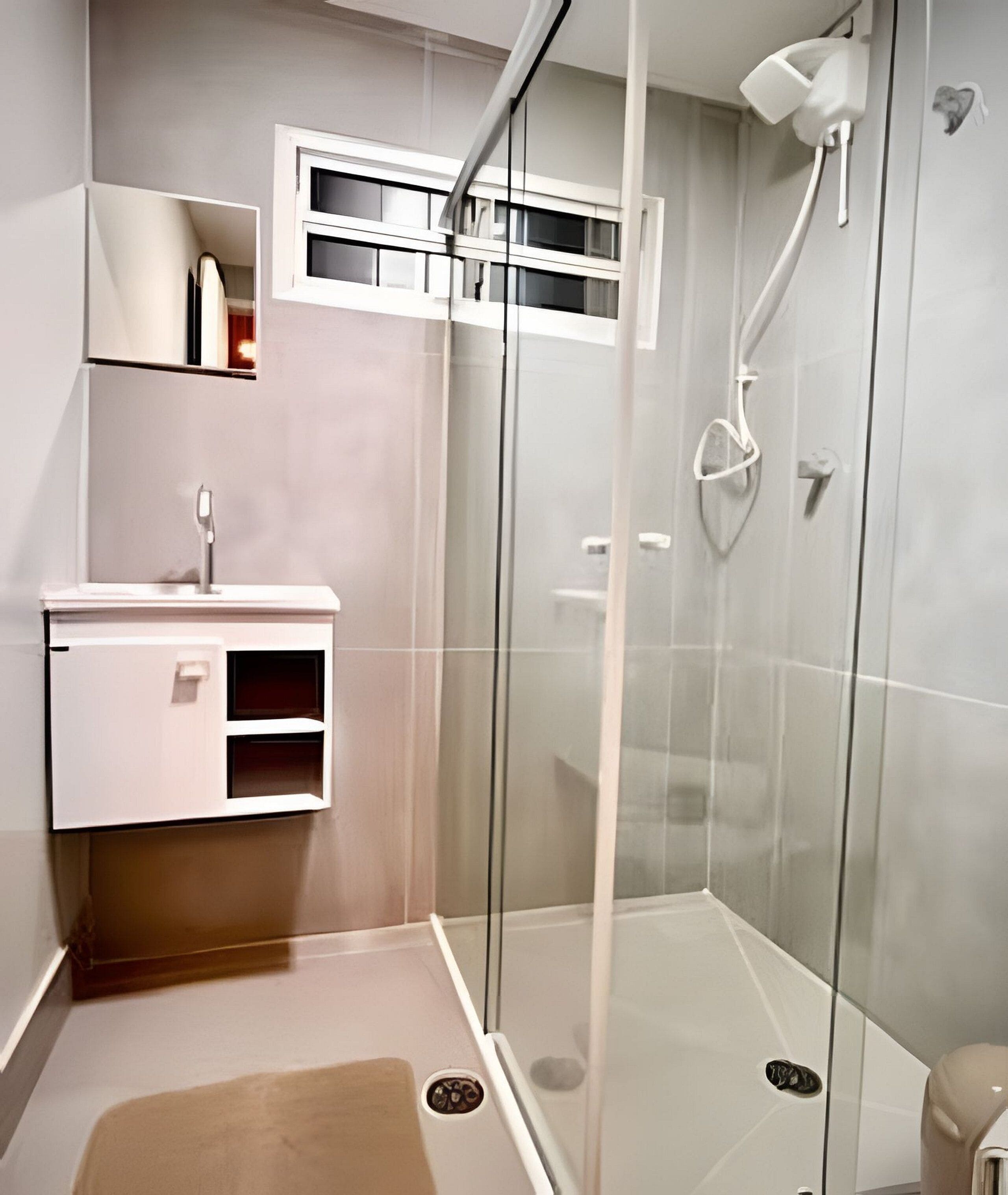 Un baño moderno con ducha de vidrio, lavamanos blanco y un espejo sobre él.