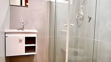 Un baño moderno con ducha de vidrio, lavamanos blanco y un espejo sobre él.