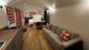 Une cuisine moderne et compacte, dotée d’un plan de travail en bois et d’appareils électroménagers intégrés, d’un canapé confortable avec des coussins à carreaux et d’un plafond incurvé agrémenté d’un éclairage encastré.