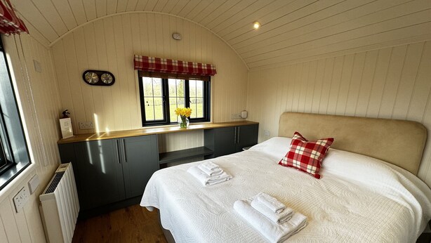 Une chambre avec un lit, une fenêtre donnant sur un beau paysage, un petit coin cuisine et un radiateur.
