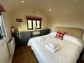 A bedroom with a bed, a window with a view, a small kitchenette, and a radiator. - The Lodge (Bromsgrove)