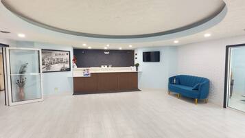 A reception area with a wooden reception desk, a blue sofa, and a wall-mounted TV.