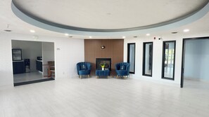A modern waiting area with a fireplace, two blue armchairs, and a coffee table. - Burgundy Inn and Suites (El Paso)